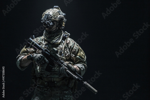 Army soldier in Combat Uniforms with assault rifle, plate carrier and combat helmet are on, Shemagh Kufiya scarf on his neck. Studio shot, dark background photo