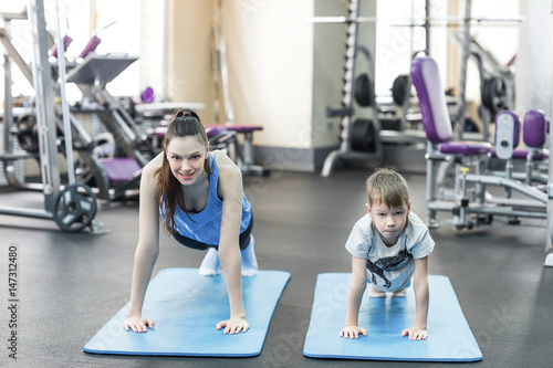 mother and son in sport shirts are doing plank in gym photo