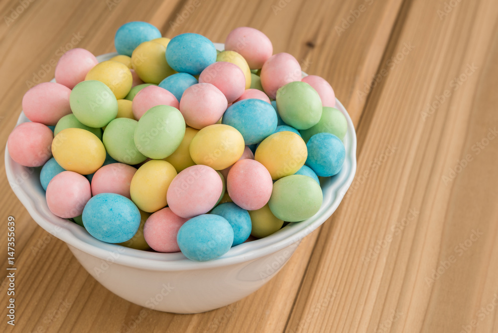 Obraz premium Bowl of pastel Easter candy eggs in a white bowl on a wood background