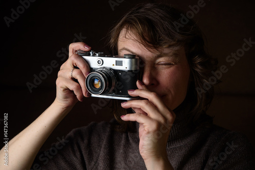 A woman is photographing a retro camera on a dark background. 