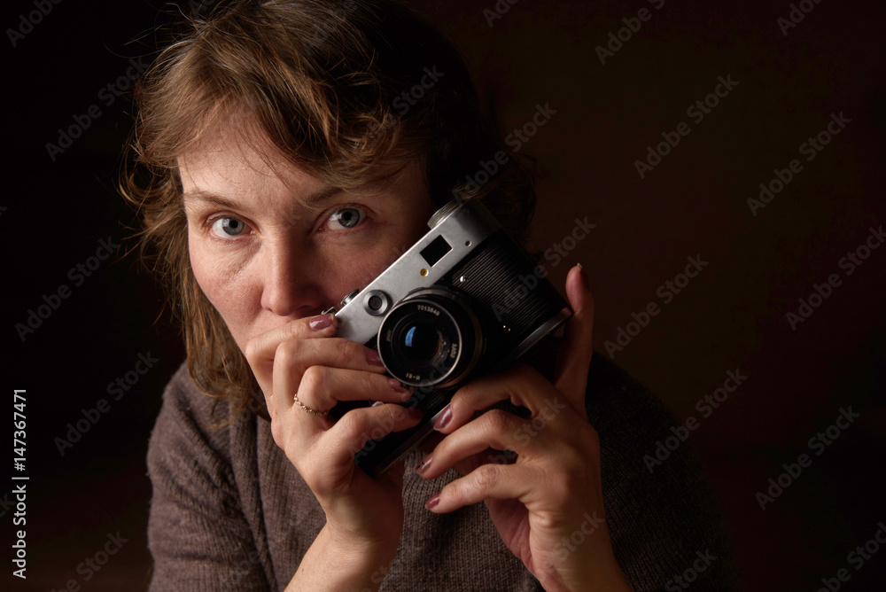 A woman is photographing a retro camera on a dark background.
A woman is photographing a retro camera on a dark background.