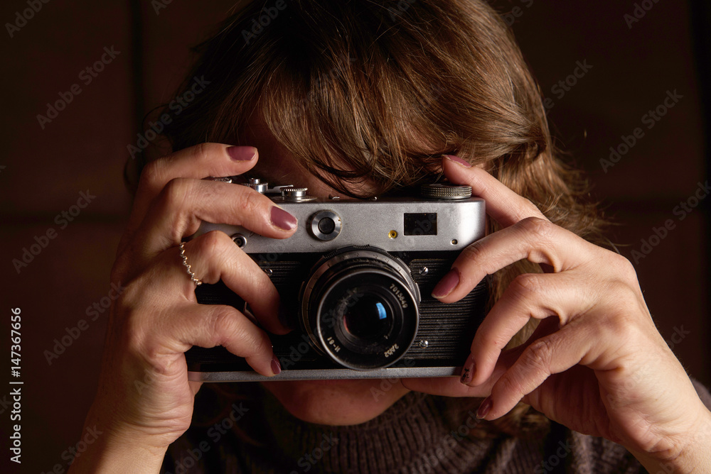 A woman is photographing a retro camera on a dark background.
A woman is photographing a retro camera on a dark background.