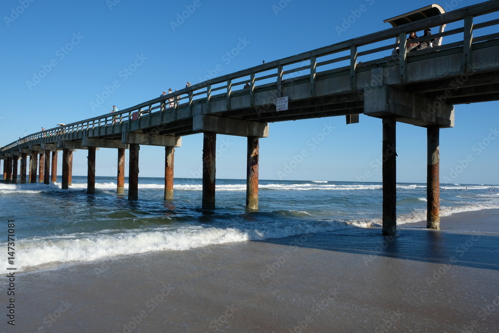 St Augustine, Florida, USA - 20 March 2017: St Augustine Beach Florida on a sunny day with no clouds.  Water laps around wood pier.  People enjoying St Johns County Ocean Pier.
