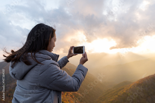 Woman taking photo on cellphone at Mount Hangetsuyama during sunset photo