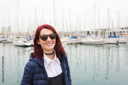 Young smiling pretty tourist woman walking on wooden pier near sea and looking at the city. HAppy Attractive hipster girl enjoying her holidays in Spain Barcelona. © nickshot