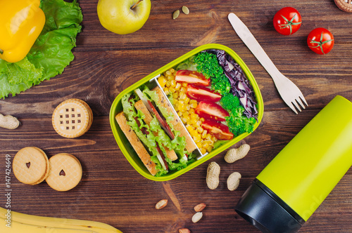 Lunch box with vegetables and sandwich near thermos mug