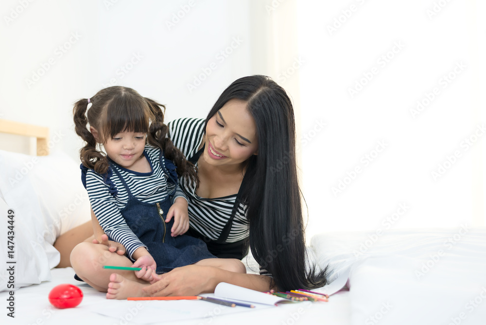 Mother looking how her child daughter drawing a picture on the bed.. Mother looking how her child daughter drawing a picture on the bed..