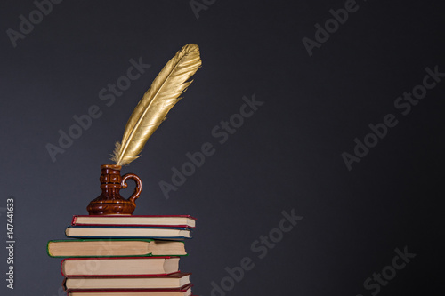 Education and information concept, literature and poetry idea. Books and inkwell with a golden quill pen on top