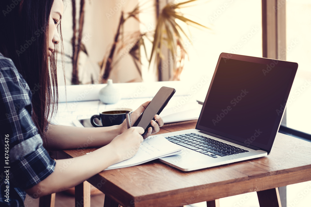 Fototapeta premium Student work process concept. Young Asisn woman working university project with generic design laptop. Analysis plans hands, using smartphone.