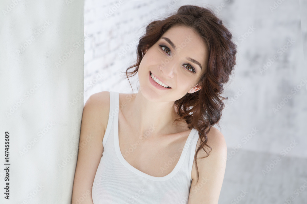 Beautiful Woman is looking at camera while standing against white brick wall Beautiful Woman is looking at camera while standing against white brick wall