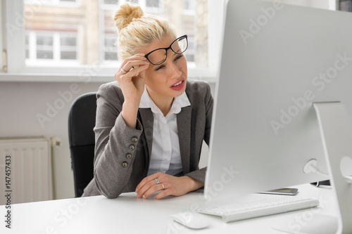 Woman at the office looking at computer with her eyes squeezed