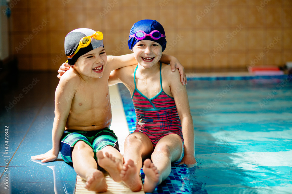 Happy children sitting on edge of the swim pool. Sport, recreation and childhood concept.