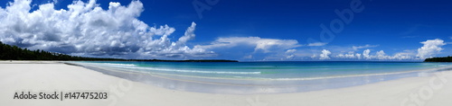 Panoramablick vom blauen Meer auf langen, weißen Sandstrand mit Palmen und dramatischen Wolken