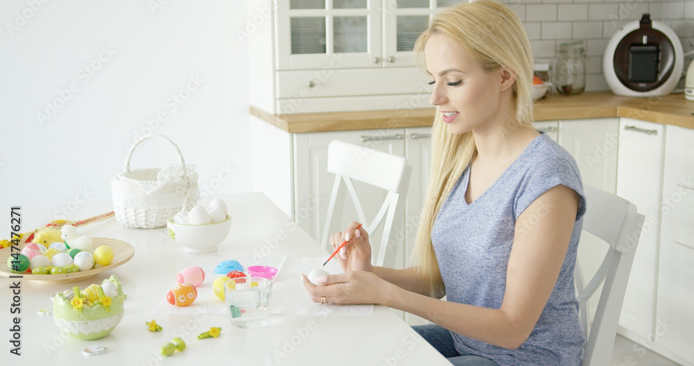 Young beautiful blonde in casual outfit sitting at table at kitchen and painting eggs for Easter holiday. Young beautiful blonde in casual outfit sitting at table at kitchen and painting eggs for Easter holiday.