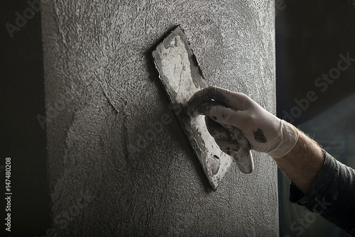 Hand of a construction worker plastering and smoothing concrete wall close-up.