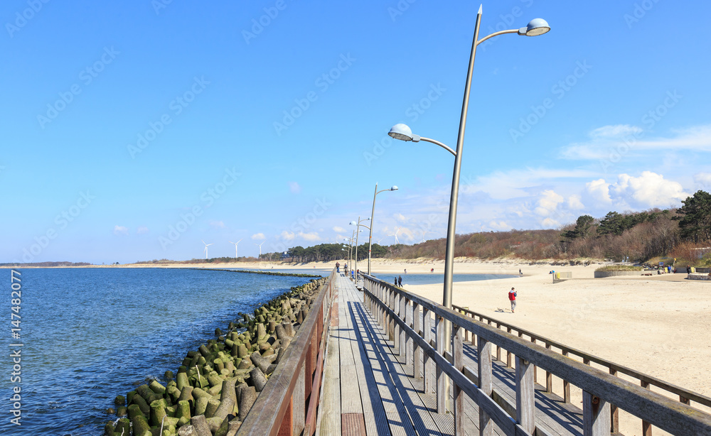 Darłówek, plaża na wybrzeżu Bałtyku. Widok infrastruktury chroniącej przed falami i służącej wypoczywającym tu ludziom