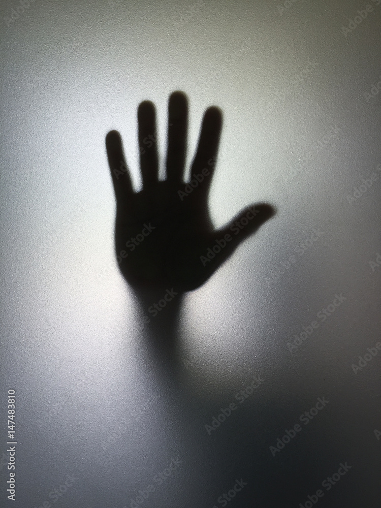 Man or woman showing stop gesture hand silhouette through frosted glass