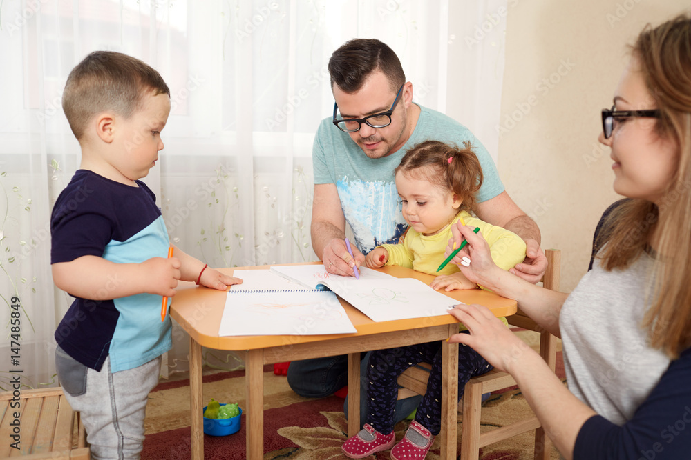The family draws pencils at a table in room. The family draws pencils at a table in room.
