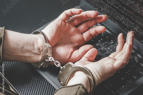 Hacker with hands behind in handcuffs on the laptop keyboard and digital code around. Cyber crime concept.