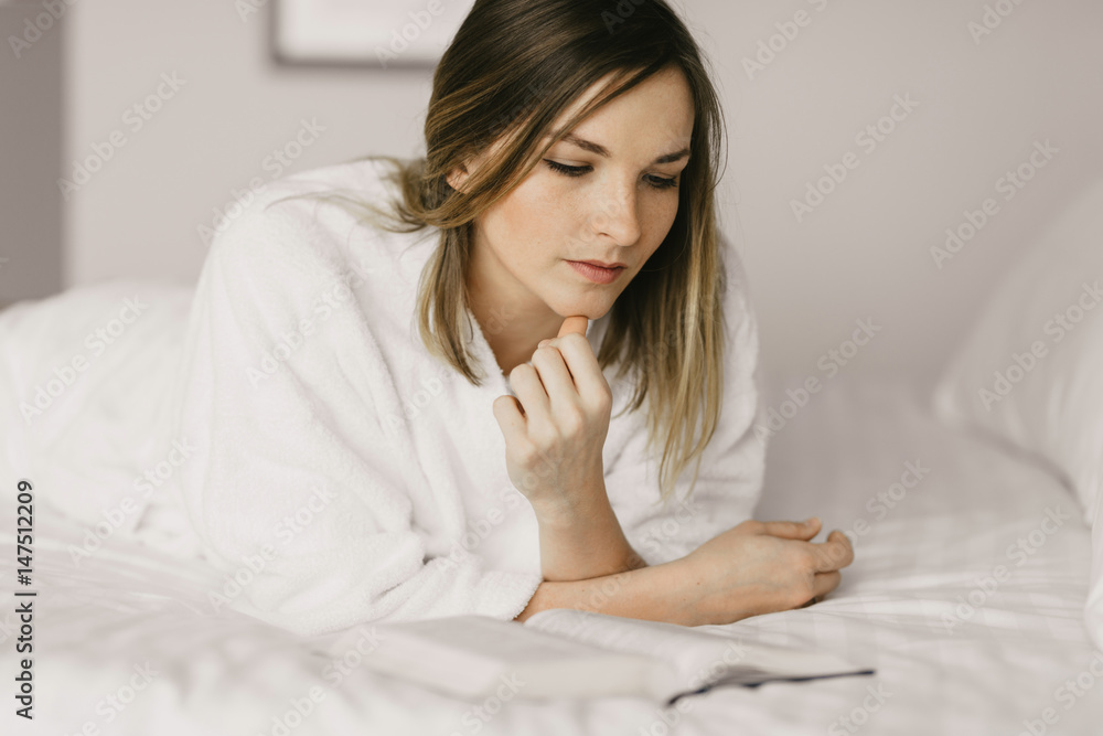beautiful woman in bathrobe lying on bed and read a book in hotel room beautiful woman in bathrobe lying on bed and read a book in hotel room