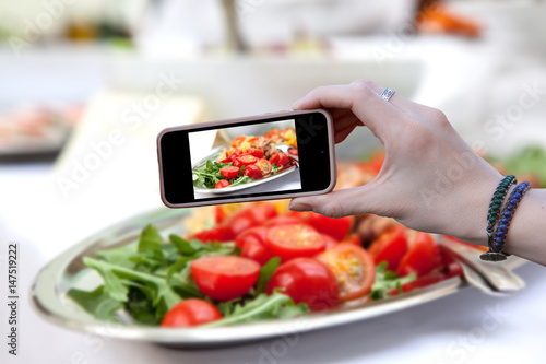 Woman holding a phone and photographed salad of red tomato