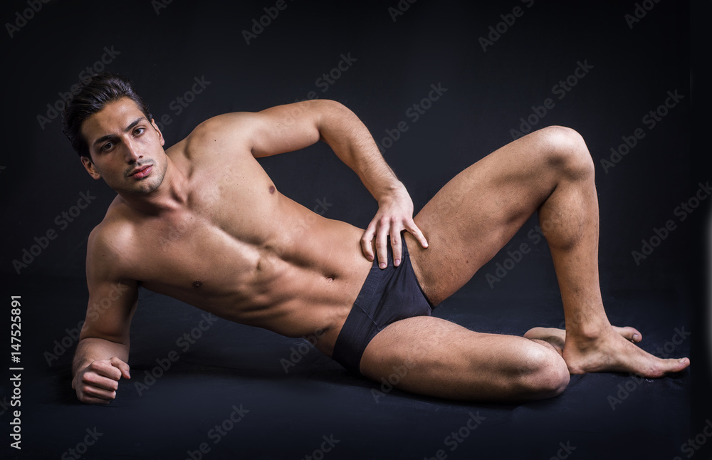 A handsome latin young man lying naked on the floor, wearing only underwear. Muscular build