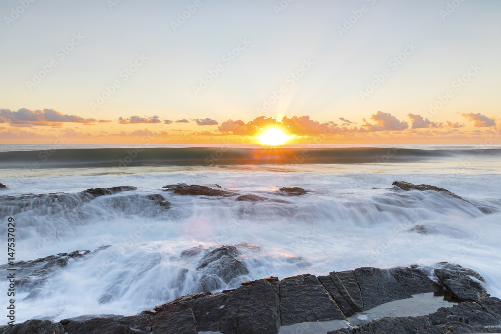Ocean sunrise with ocean cascading over the end of Currumbin Rock. Gold Coast.