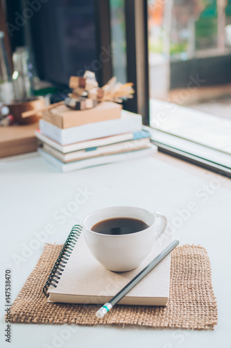 Cup of hot coffee and brown note book on table.