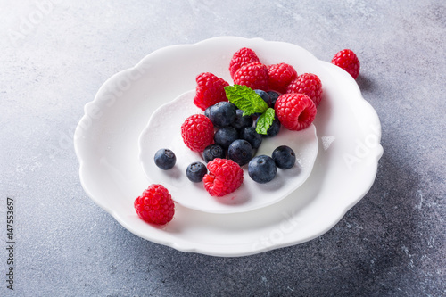 Freshly picked blueberries and raspberries on white plate on gray stone background. Concept for healthy eating and nutrition with copy space.