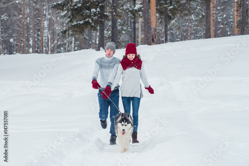 Young couple with a Husky dog walking in winter park, man and woman playing and having fun with dog.