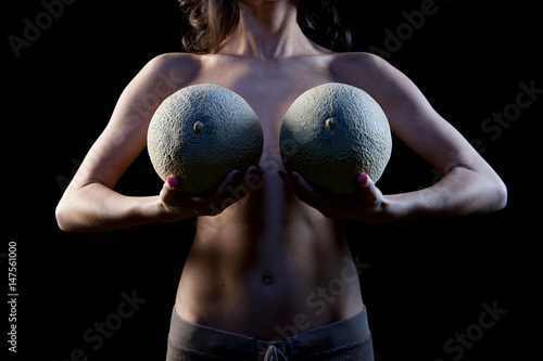 Woman holding cataloupe melons in front of breasts photo