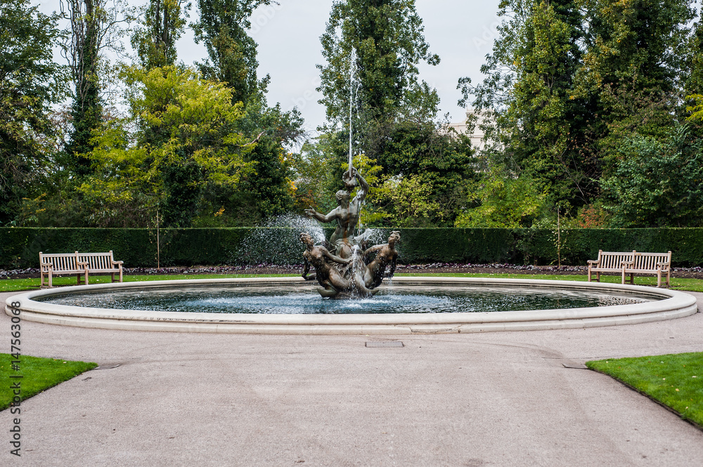 Fountain in London Park, squirting water all the way with benches on sides