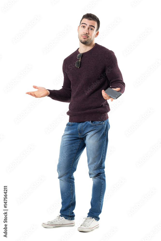 Clueless young casual man shrugging shoulders holding mobile phone ...