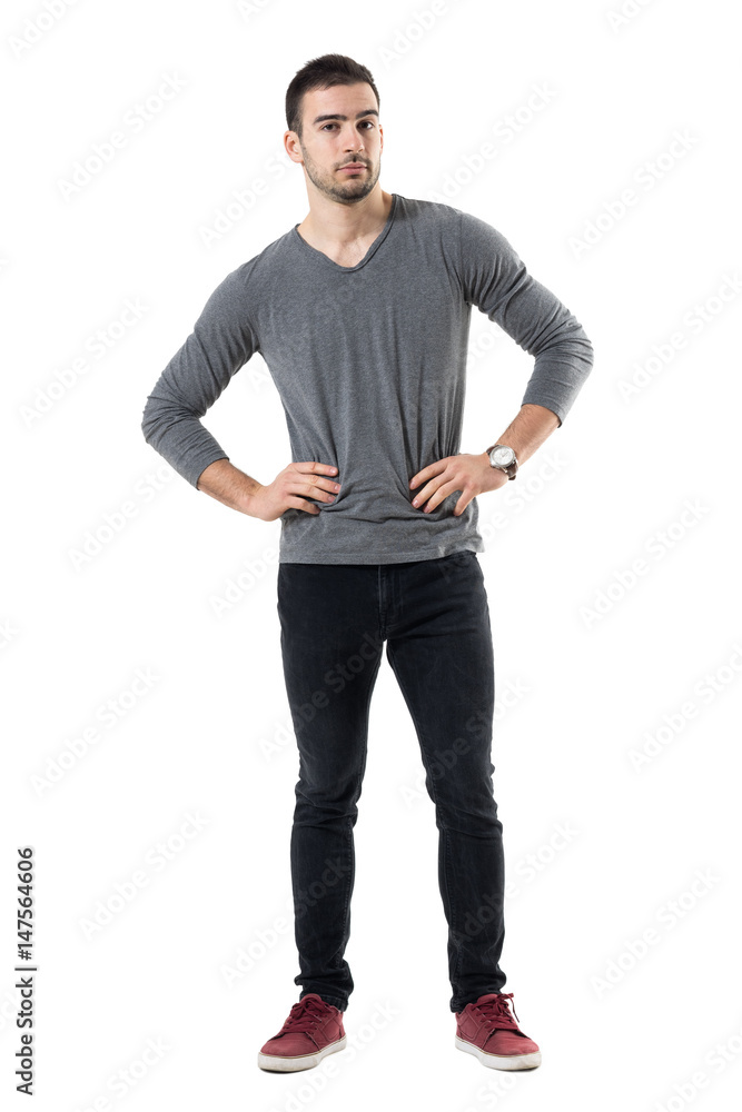 Serious young casual man with hands on waist looking at camera. Full body length portrait isolated over white studio background. Serious young casual man with hands on waist looking at camera. Full body length portrait isolated over white studio background.