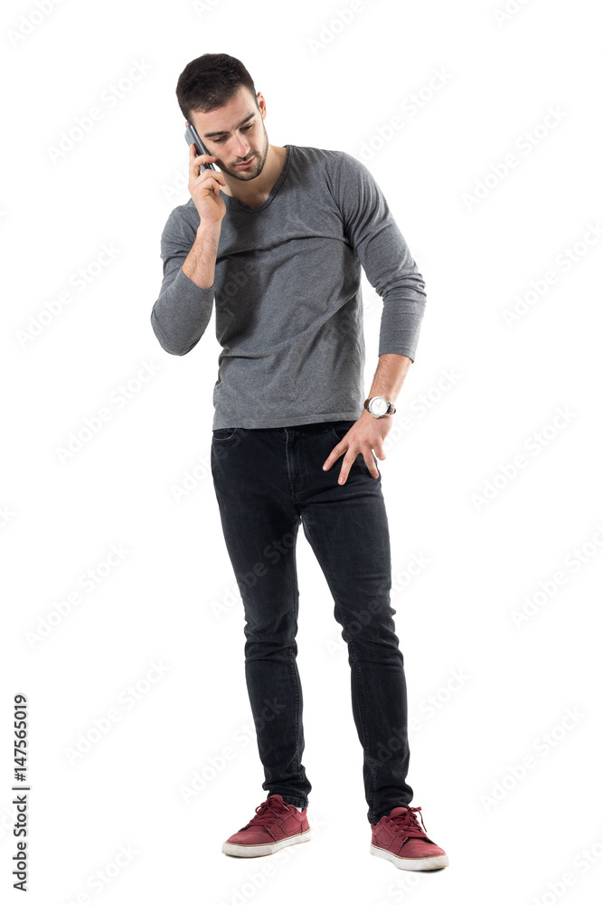 Serious young worried casual man talk on the phone looking down. Full body length portrait isolated over white studio background. Serious young worried casual man talk on the phone looking down. Full body length portrait isolated over white studio background.