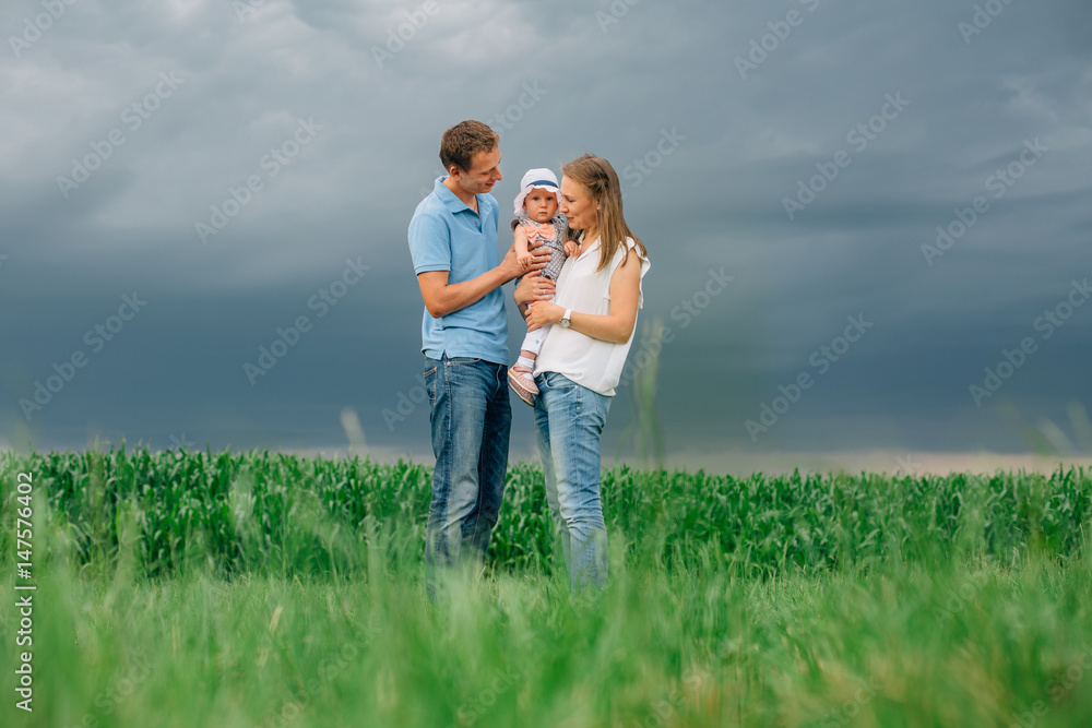 Mother and father holding little daughter standing in the green field. Thunder sky. Happy family concept. Mother and father holding little daughter standing in the green field. Thunder sky. Happy family concept.