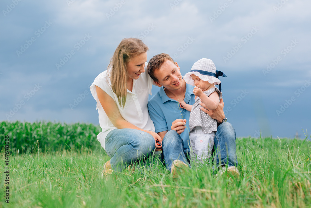 Young family in jeans sitting on the grass having fun together. Little girl in panama hat. Young family in jeans sitting on the grass having fun together. Little girl in panama hat.