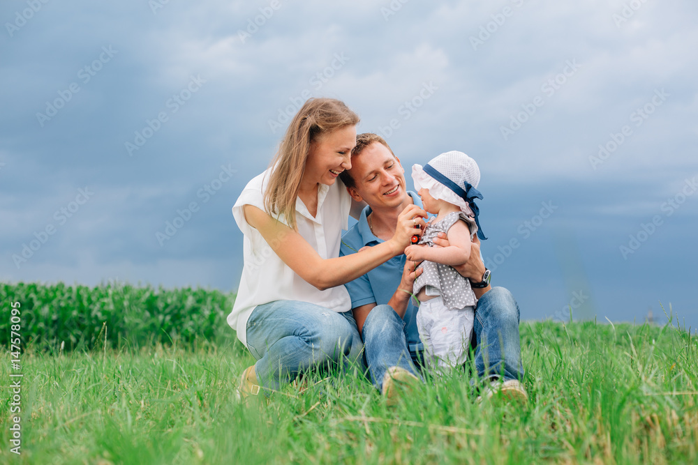 Young family in jeans sitting on the grass having fun together. Little girl in panama hat. Young family in jeans sitting on the grass having fun together. Little girl in panama hat.