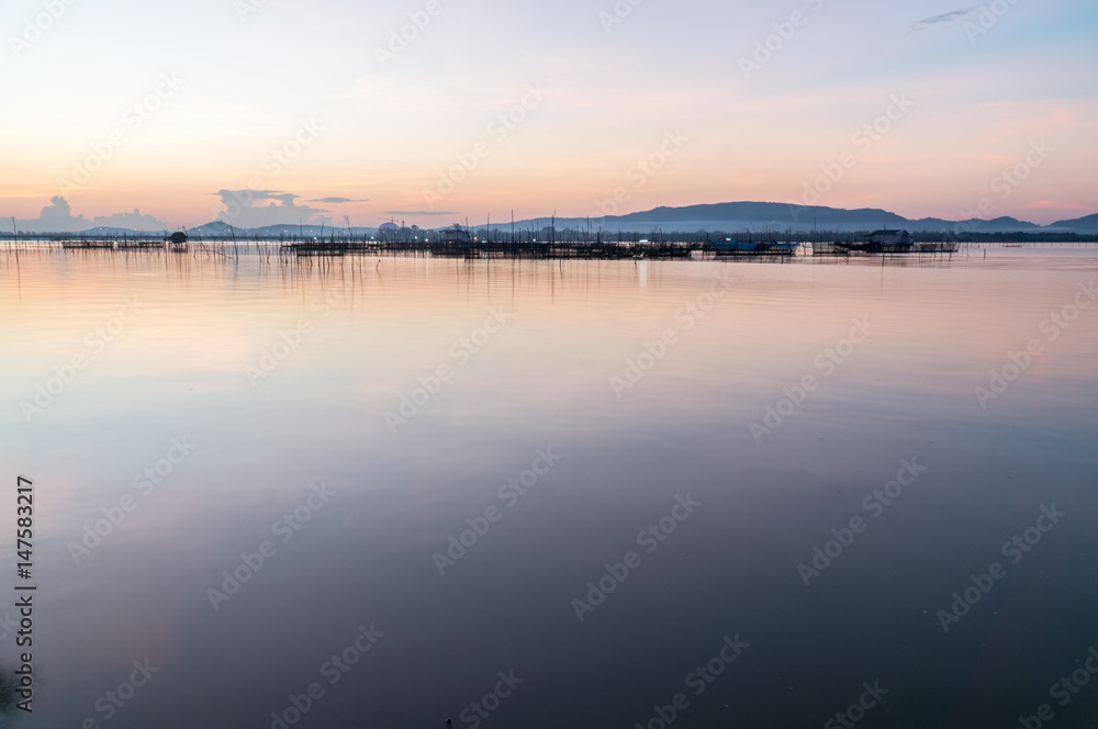 Fisherman hut in the middle of Songkhla lake with beautiful twilight sky reflecting on water surface and mountain in background.