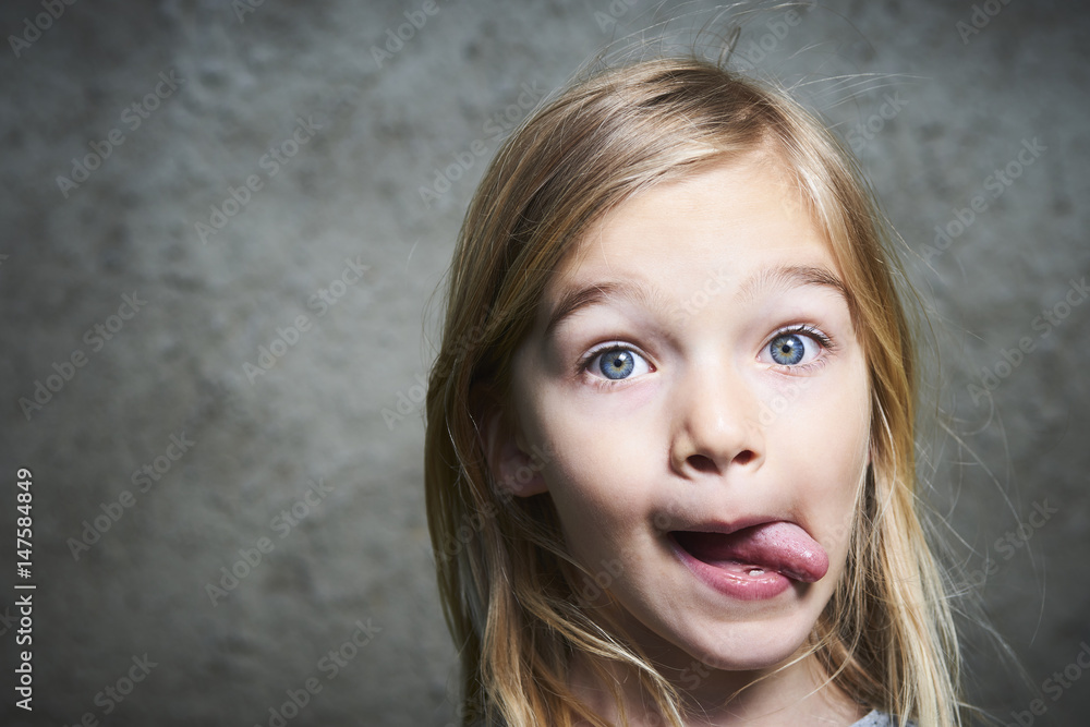 little child blond girl making faces with gray grunge wall background