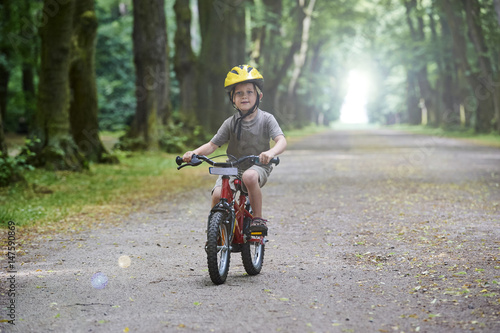 Child boy on a bicycle in the forest in summer. Boy cycling outdoors in safety helmet. Sun flare effect added © Petr Bonek