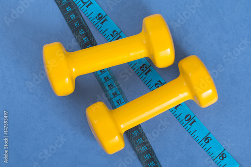 Pair of yellow dumbbells and tape measure on a blue surface.