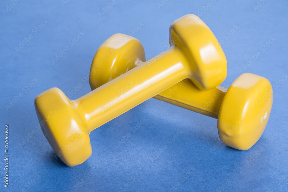 Pair of yellow dumbbells on a blue surpface. Pair of yellow dumbbells on a blue surpface.