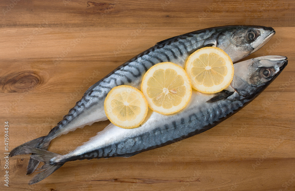Pair of fresh mackerel with slices of lemon on wooden board surface. Top view, close up. Pair of fresh mackerel with slices of lemon on wooden board surface. Top view, close up.