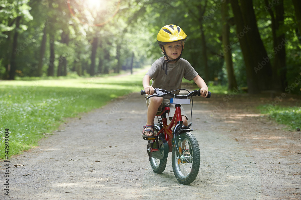 Fototapeta premium Child boy on a bicycle in the forest in summer. Boy cycling outdoors in safety helmet. 