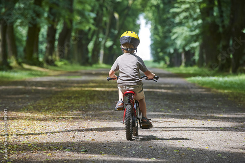 Child boy on a bicycle in the forest in summer. Boy cycling outdoors in safety helmet.  © Petr Bonek