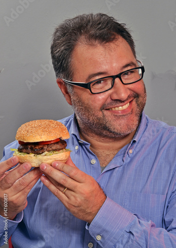 Hombre gordo feliz comiendo hamburguesa y patatas fritas.