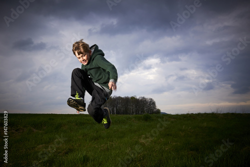 Child blond boy jumping in a spring green meadow against a storm's cloudy sky at sunset   © Petr Bonek