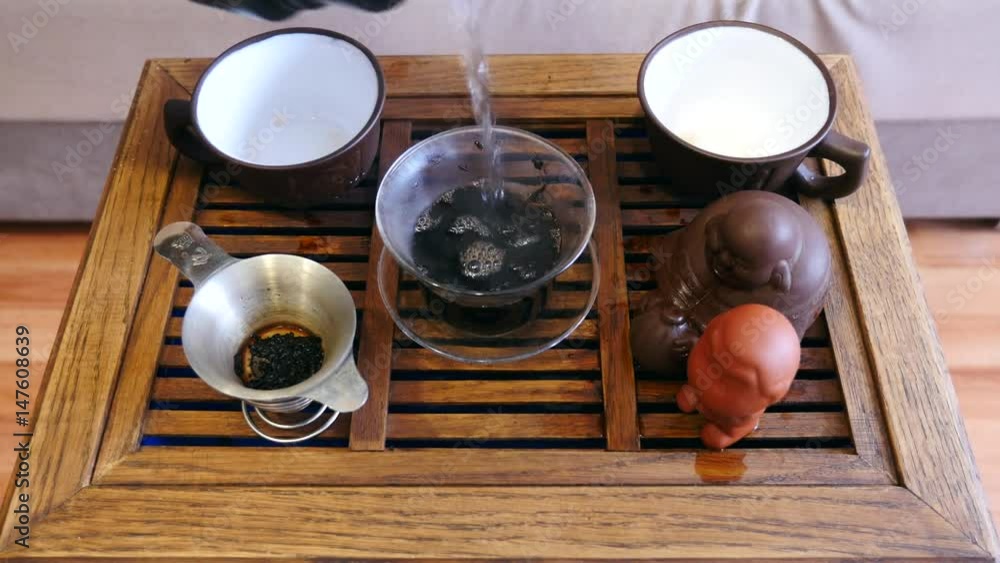 The action of traditional Chinese tea ceremony. Pouring tea from covered bowl in a cup. Wooden tea board on the background. The action of traditional Chinese tea ceremony. Pouring tea from covered bowl in a cup. Wooden tea board on the background.