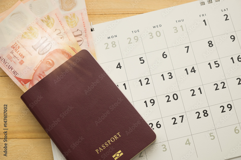 top view. passport have singapore cash inside putting on desktop calendar wooden are background. this image for business,travel and finance concept top view. passport have singapore cash inside putting on desktop calendar wooden are background. this image for business,travel and finance concept